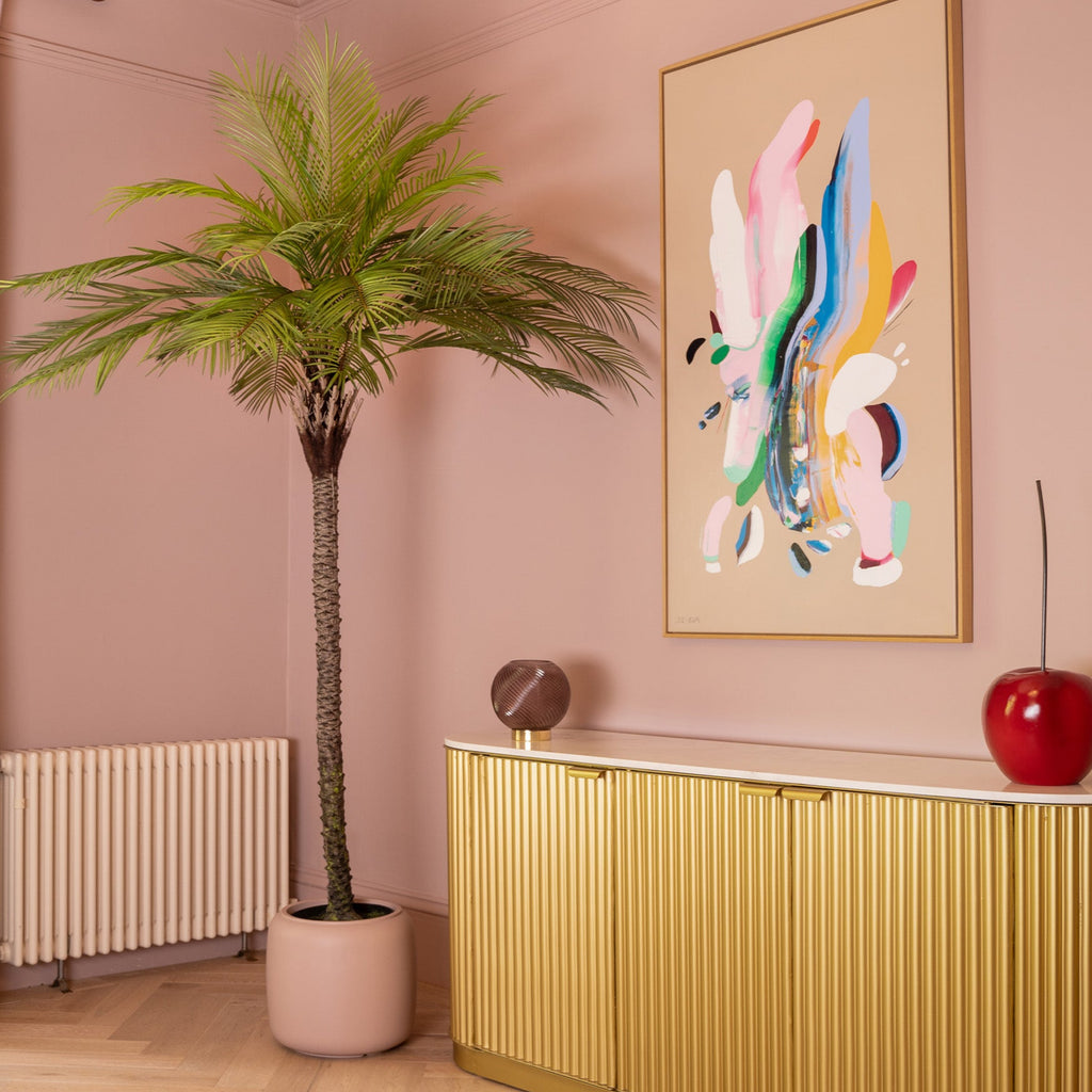 Modern interior with a gold console table, abstract art, and decorative items against a pink wall.