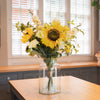 Bouquet of sunflowers and white flowers in a clear vase on a kitchen counter.