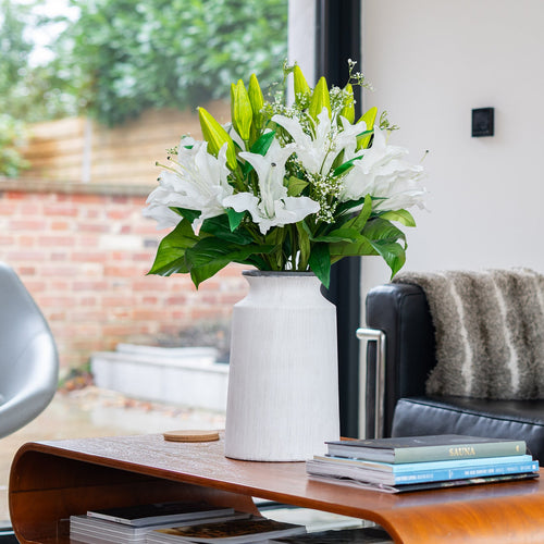 Living room with a vase of flowers on a coffee table, books underneath, and a couch with a blanket.