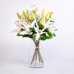 Bouquet of white and yellow flowers in a clear vase on a light gray background