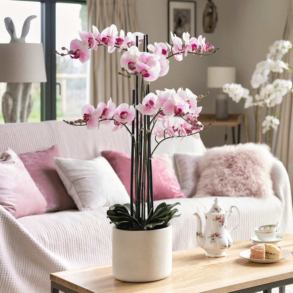 Living room with pink orchids on a coffee table, white sofa, and large windows.