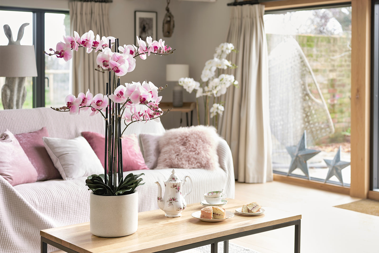 Living room with artificial pink orchids on a coffee table, white sofa, and large windows.