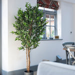 Artificial potted tree in a room with a window and dining area.