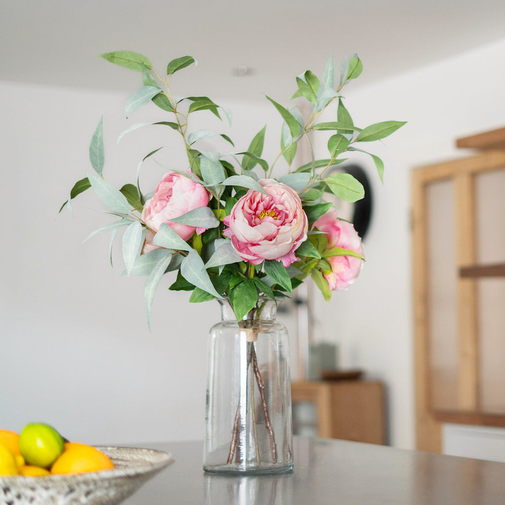 Clear vase with pink flowers and green leaves on a kitchen counter.