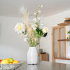 White vase with flowers on a table in a room with a blurred background