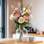 Bouquet of flowers in a clear vase on a table with two cups in a kitchen setting.