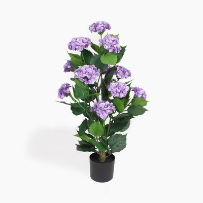 An artificial hydrangea plant with purple flowers and green leaves, potted in a black plastic pot, shown against a plain white background.