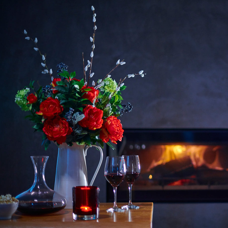 Floral arrangement with wine glasses and a candle on a table in front of a fireplace.