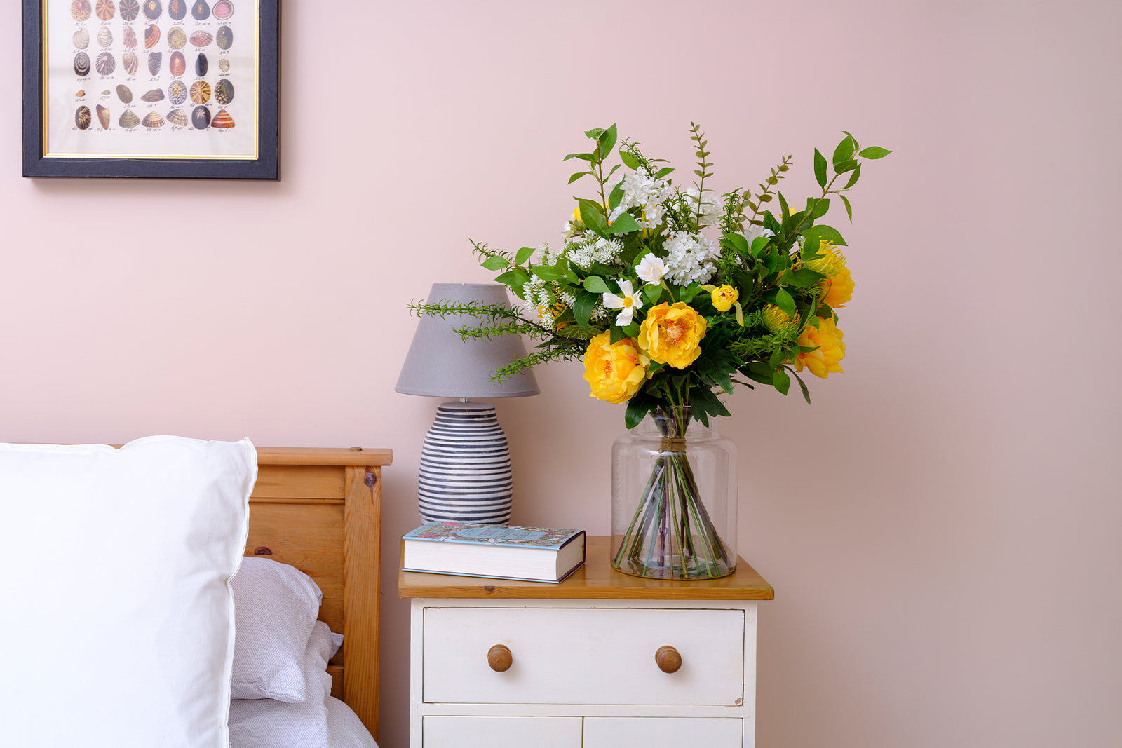 Floral arrangement on a nightstand next to a bed with a pink wall in the background