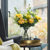 Bouquet of yellow flowers in a clear vase on a small round table with a star decoration, in front of a glass door.