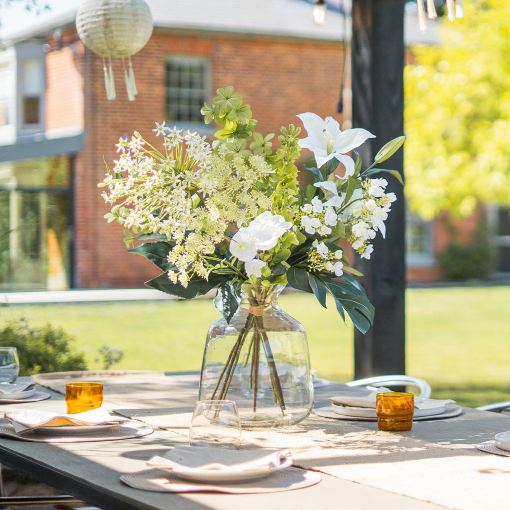 Bouquet of white and green flowers in a clear vase on an outdoor table with a blurred background