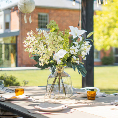 Bouquet of white and green flowers in a clear vase on an outdoor table with a blurred background