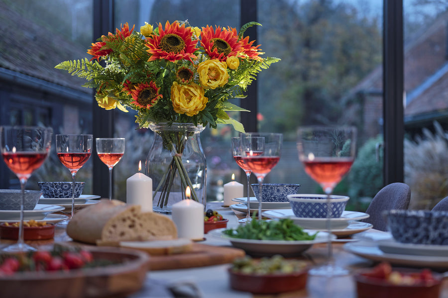 Dining table set with flowers, candles, and wine glasses outdoors.
