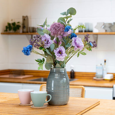 Vase with flowers on a kitchen counter with two mugs.