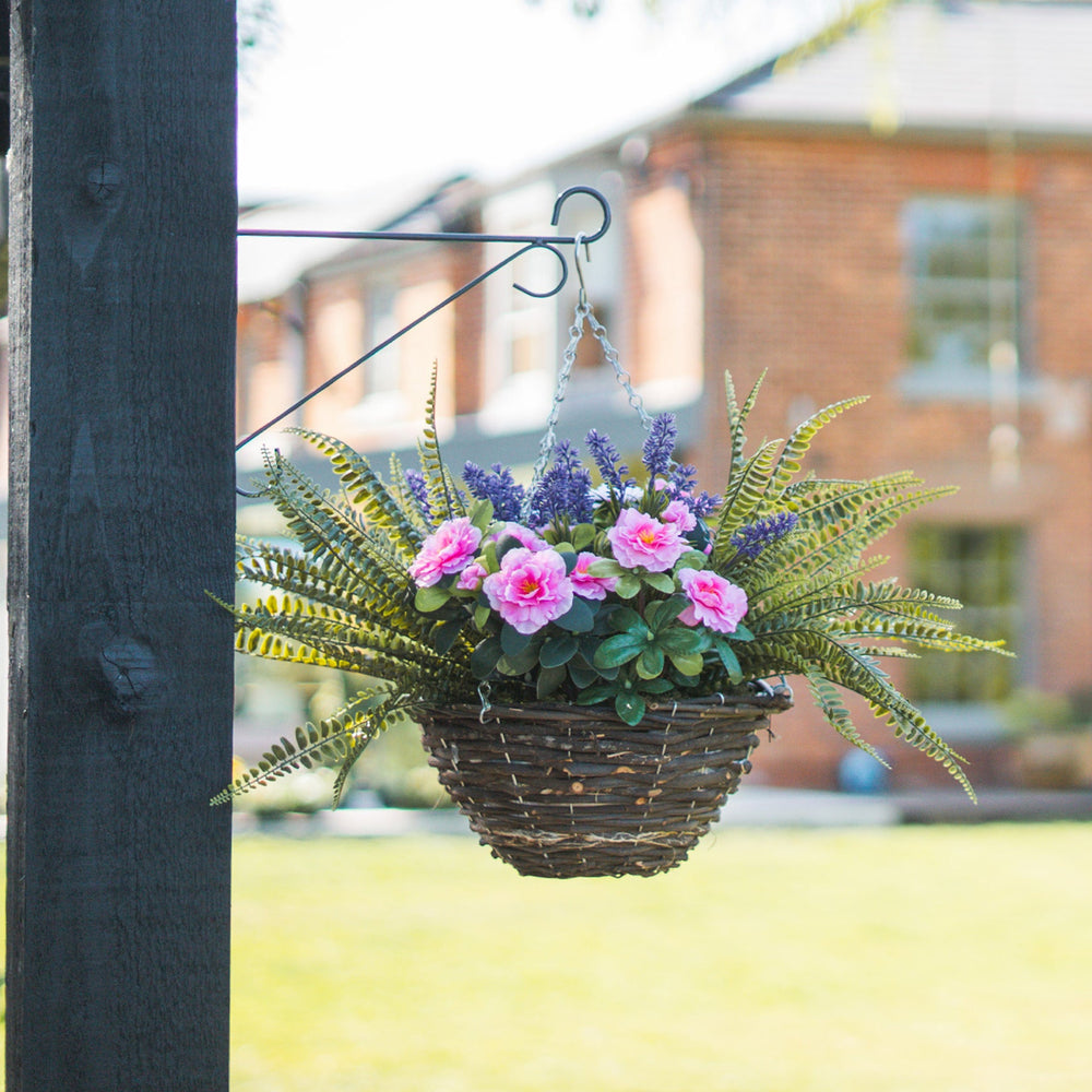 Hanging basket with flowers and ferns attached to a wooden post outdoors.