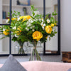 Vase of yellow flowers in front of a decorative mirror on a wall.
