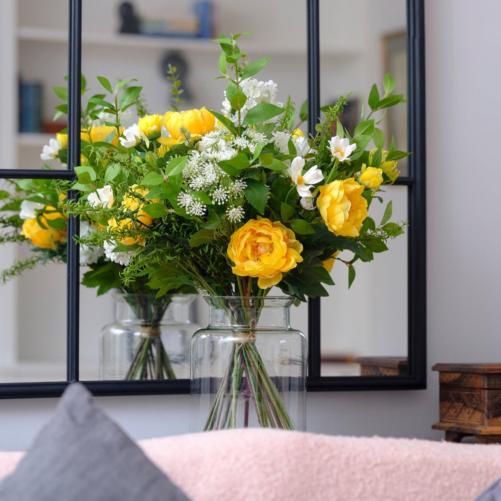 Vase of yellow flowers in front of a decorative mirror on a wall.