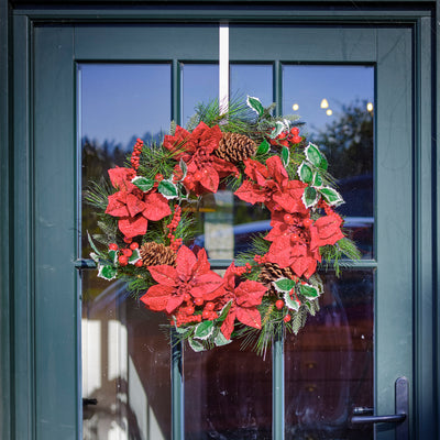 Christmas wreath with red flowers and pine cones on a glass door