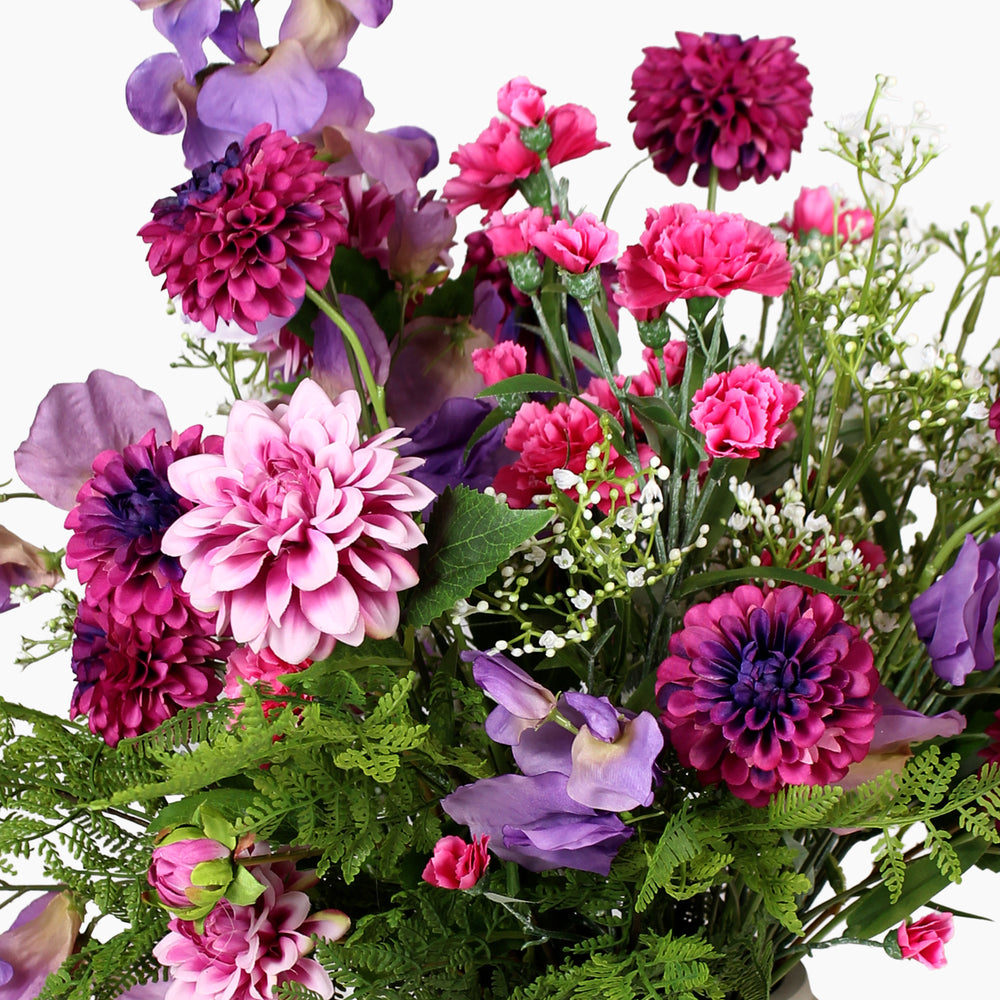 A dense, vibrant artificial flower bouquet featuring pink and purple with green foliage, set against a plain white background.