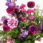 A dense, vibrant artificial flower bouquet featuring pink and purple with green foliage, set against a plain white background.