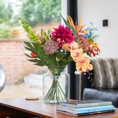 Colorful bouquet of flowers in a vase on a wooden table with a black leather sofa and window in the background.
