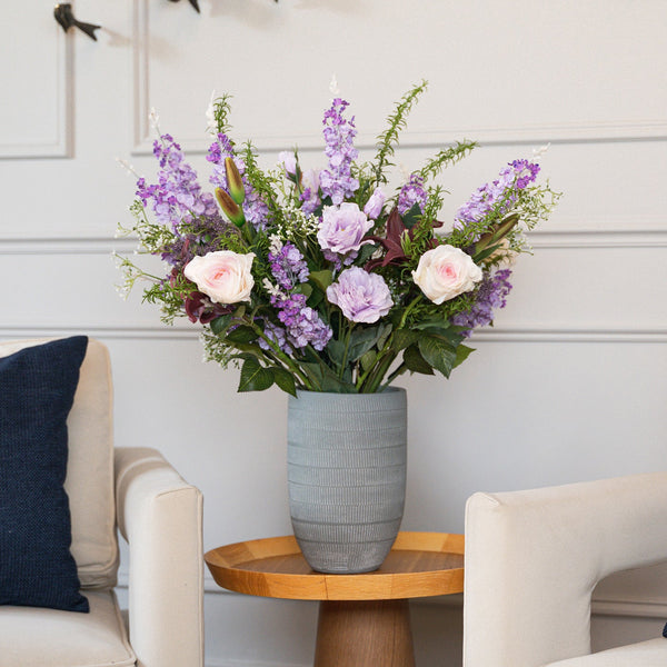 Floral arrangement in a vase on a wooden side table between two chairs with blue cushions.