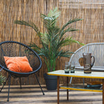 Outdoor patio with wicker chair, table, and plants against a bamboo wall.