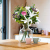 Bouquet of flowers in a clear vase on a wooden table with a kitchen background