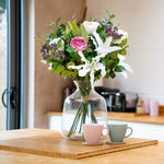 Bouquet of flowers in a clear vase on a wooden table with a kitchen background