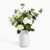 Bouquet of white flowers and greenery in a white vase on a white background