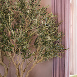 Artificial olive tree with green leaves and black olives against a pink curtain background