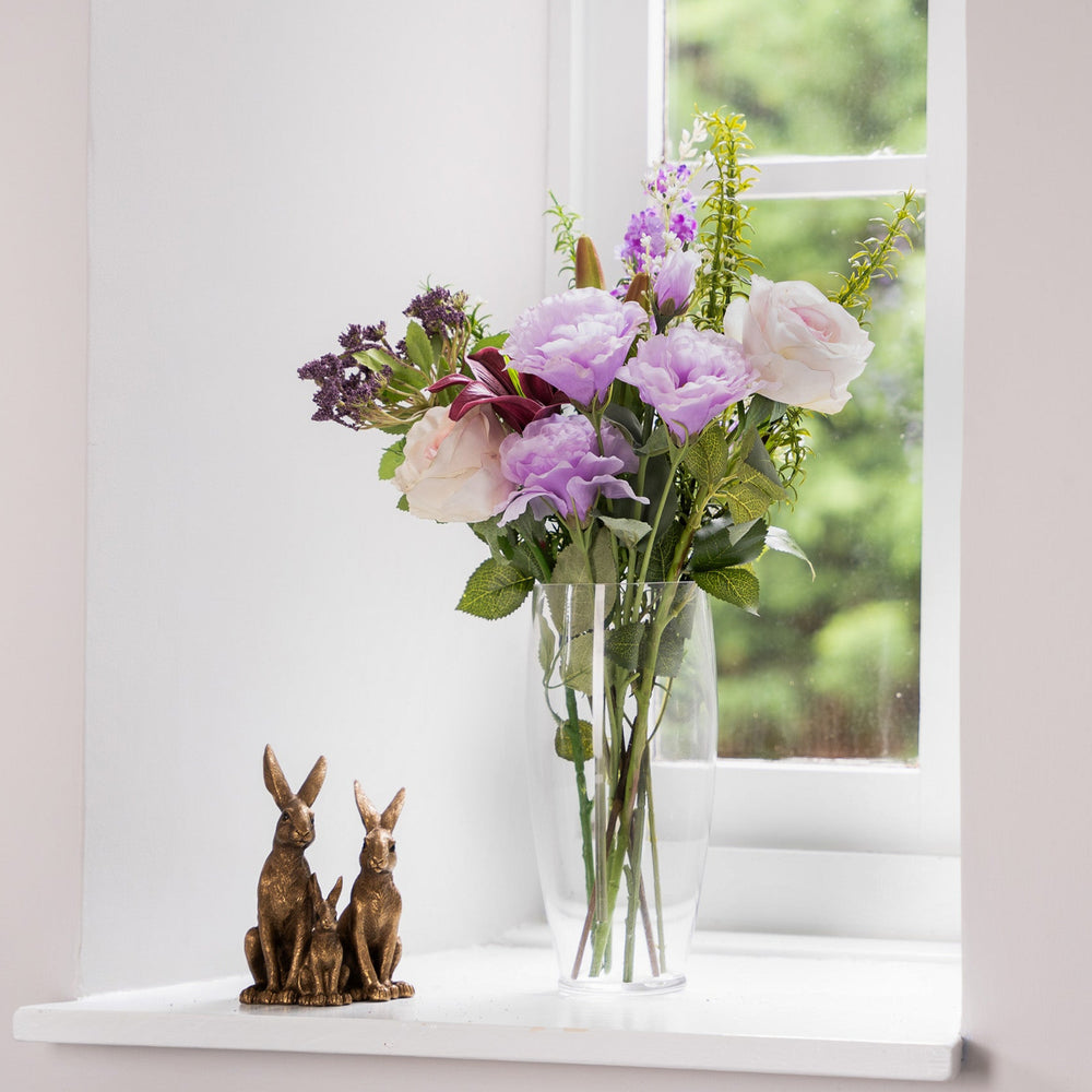 Bouquet of flowers in a vase on a windowsill with two rabbit figurines.