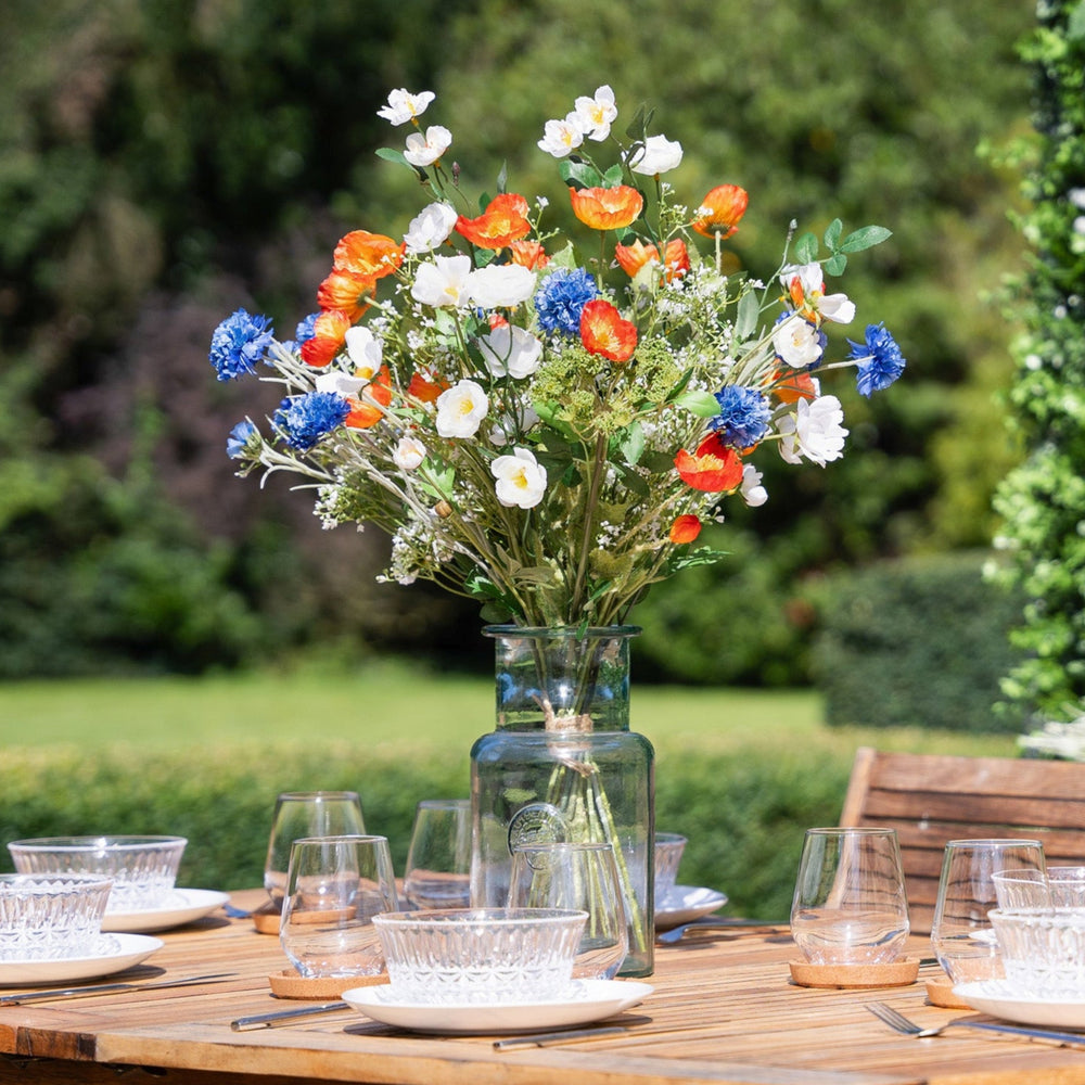 Outdoor setting with a wooden table set for a meal, featuring a vase of colorful flowers.