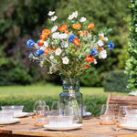 Outdoor setting with a wooden table set for a meal, featuring a vase of colorful flowers.