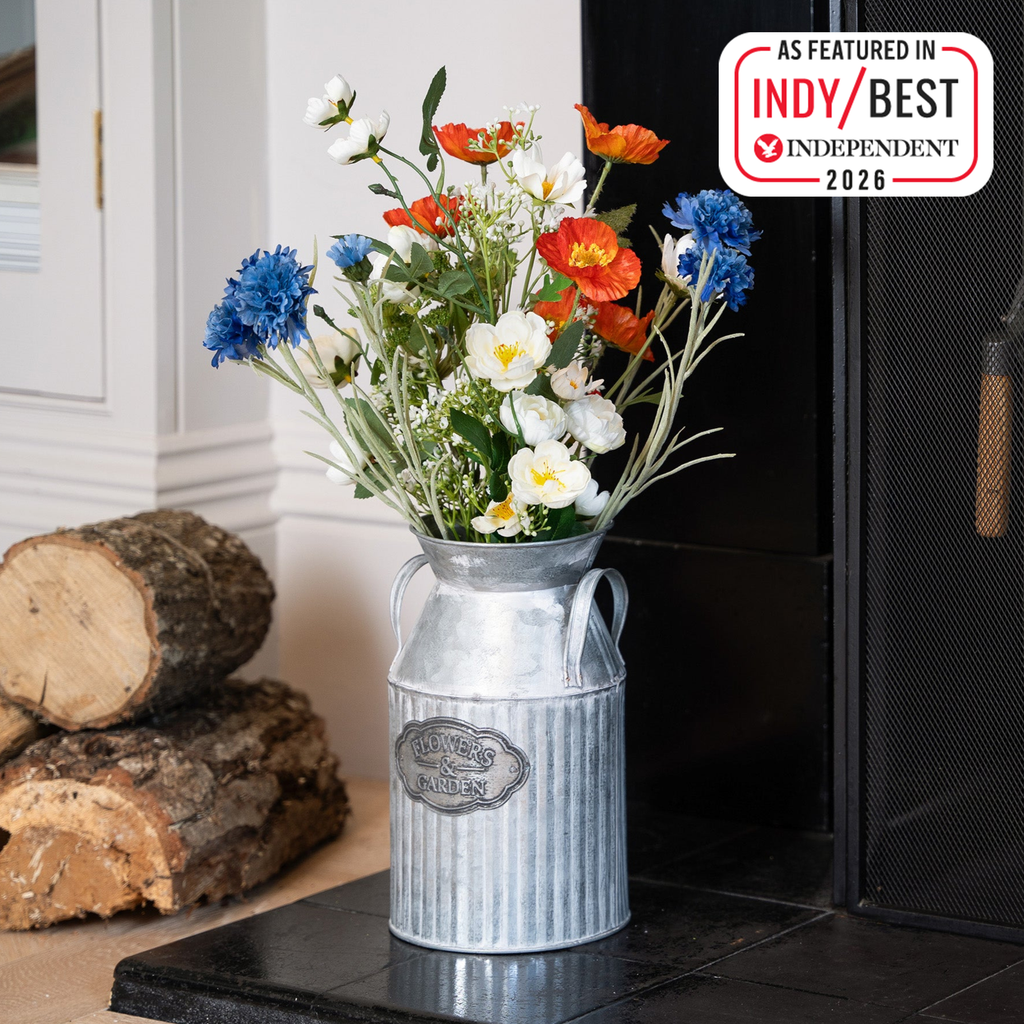 Decorative milk churn with flowers on a hearth next to stacked logs featuring 'IndyBest Independent 2026' badge.