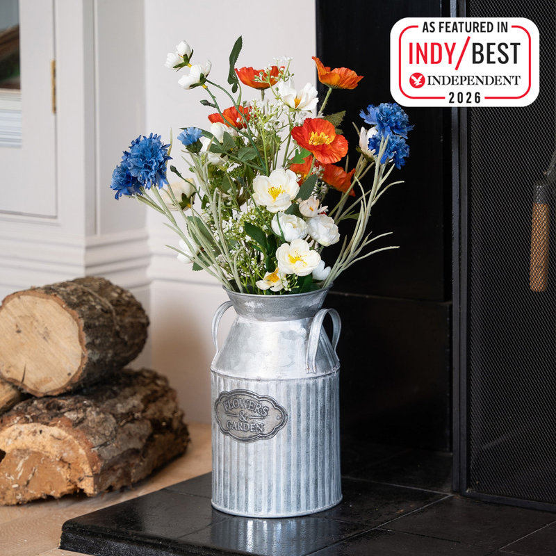 Decorative milk churn with flowers on a hearth next to stacked logs featuring 'IndyBest Independent 2026' badge.