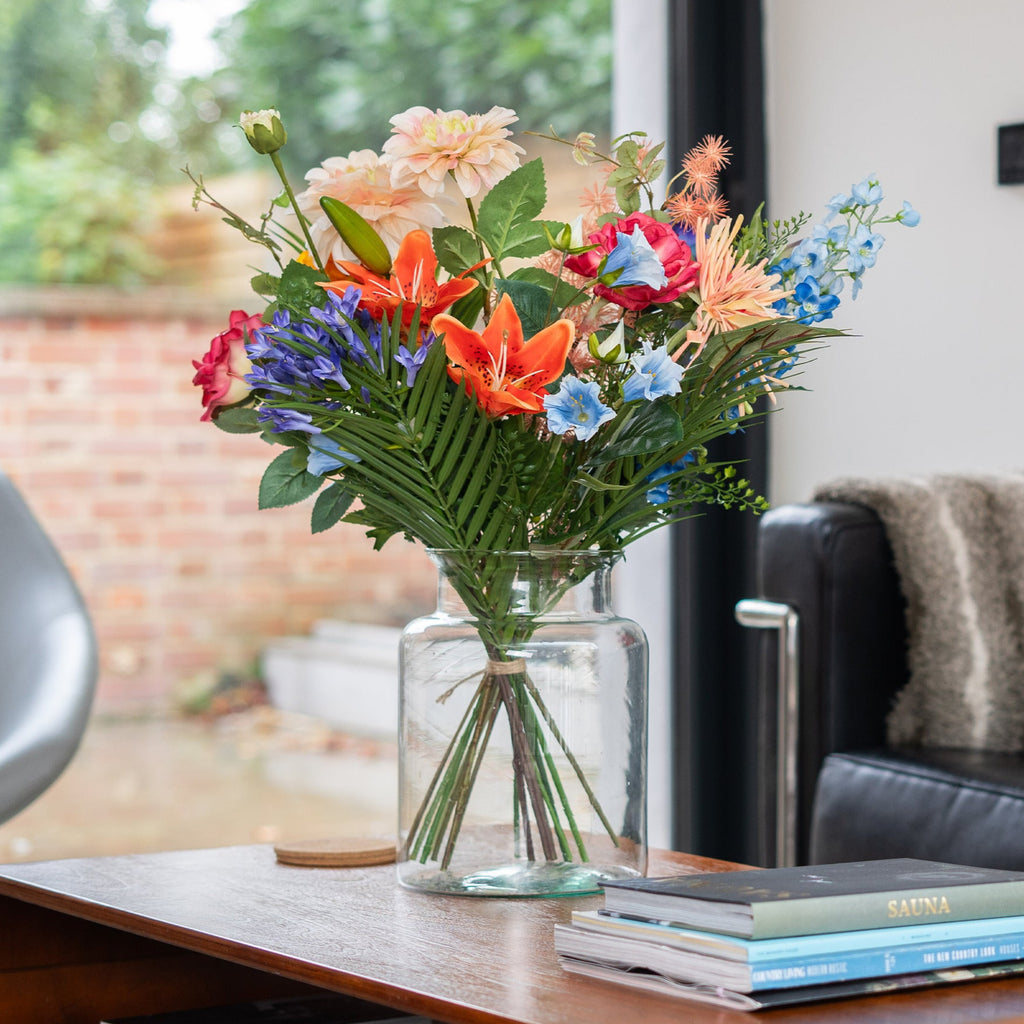 Colorful bouquet of flowers in a vase on a wooden table with a couch and window in the background
