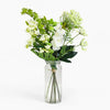 Bouquet of green and white flowers in a clear glass vase on a white background