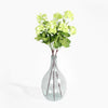 Clear glass vase with green artificial flowers on a white background