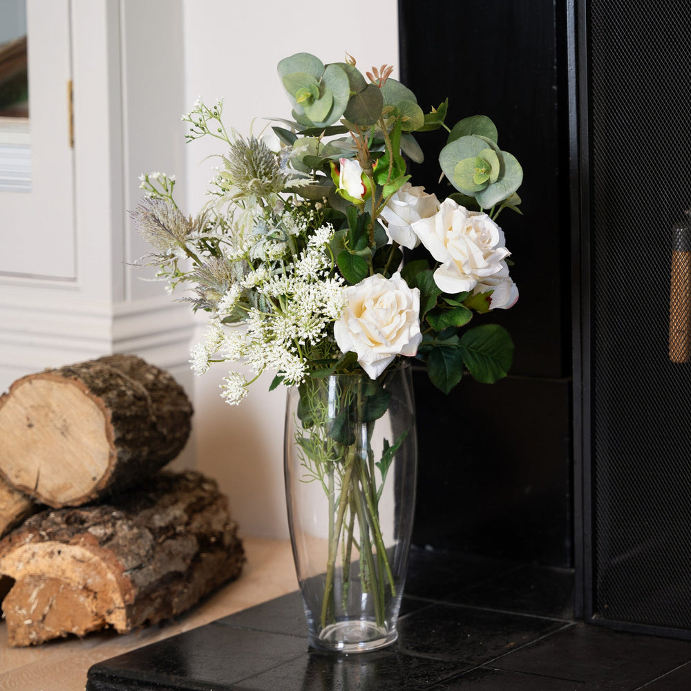 Vase with flowers on a fireplace hearth next to stacked logs