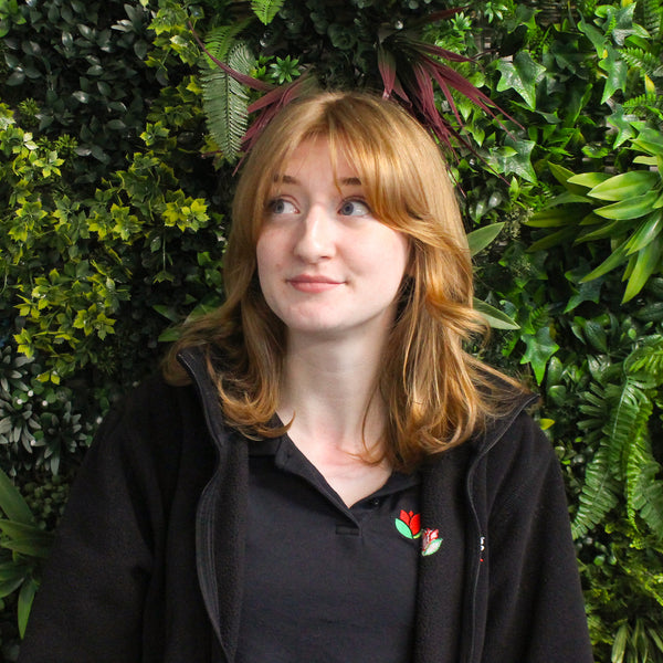 Person wearing a black jacket with a red flower emblem against a green leafy background