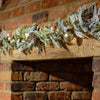Decorative greenery with gold ornaments on a wooden mantel against a brick wall.