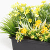 Close up of artificial planter with yellow flowers in a black pot on a white background