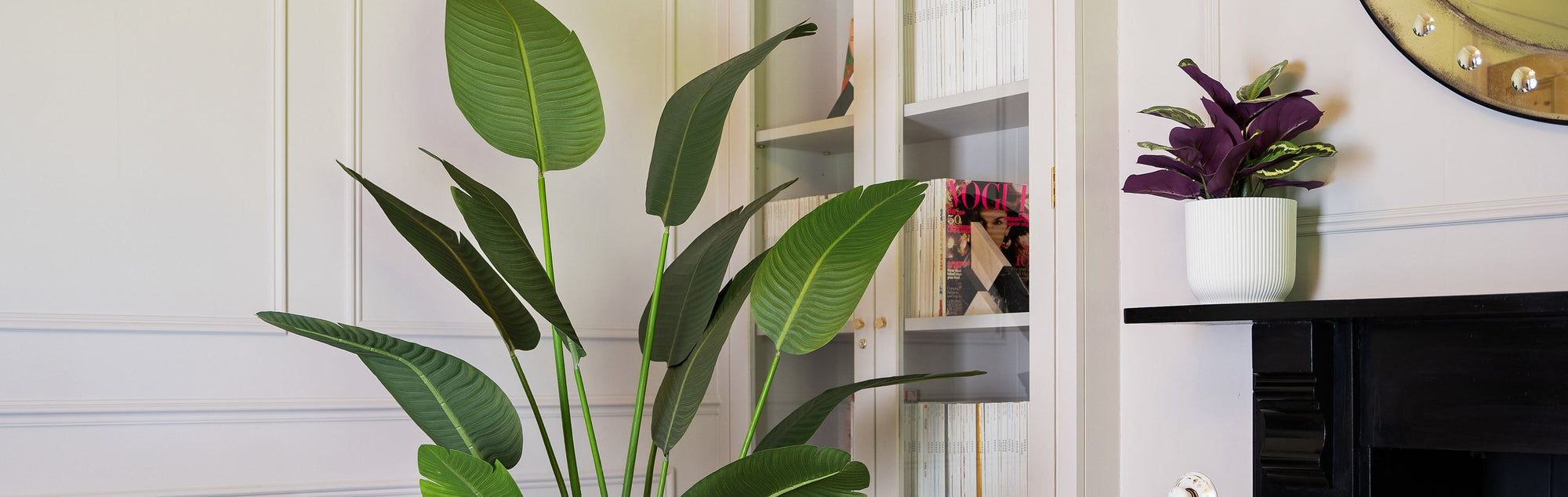 Living room with a large artificial strelitzia, bookshelf, and fireplace.
