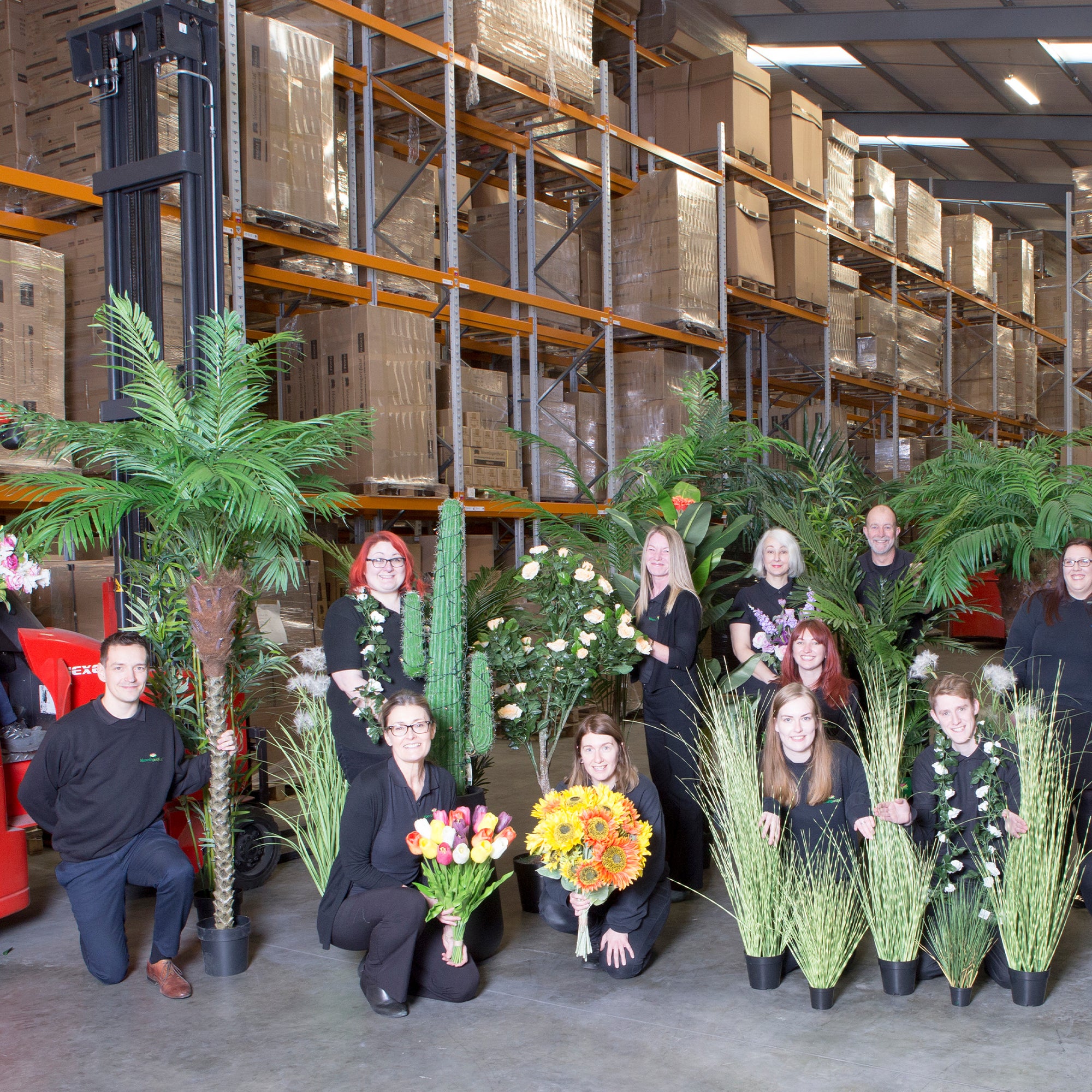 Group of people in a warehouse with floral arrangements and plants.