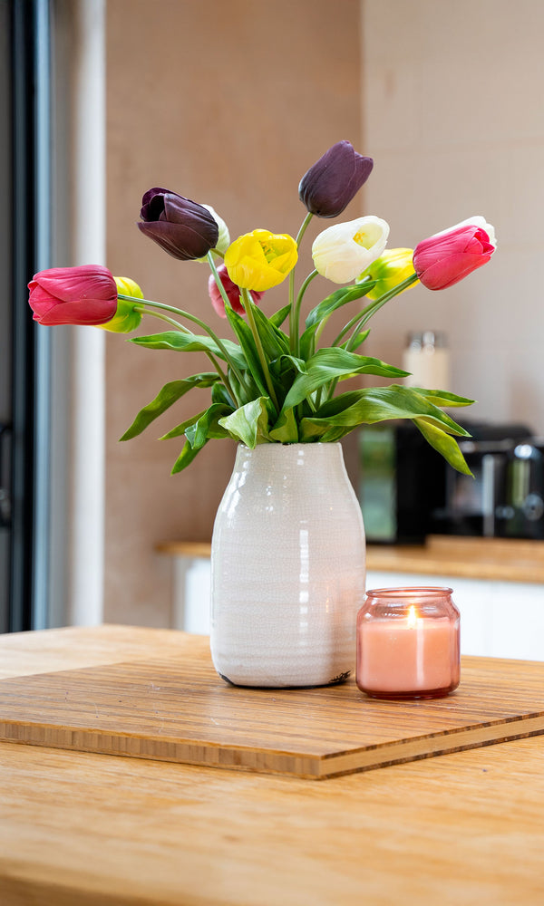 Artificial tulips arrangements in white vase on wooden kitchen countertop with a blurred kitchen in background. 
