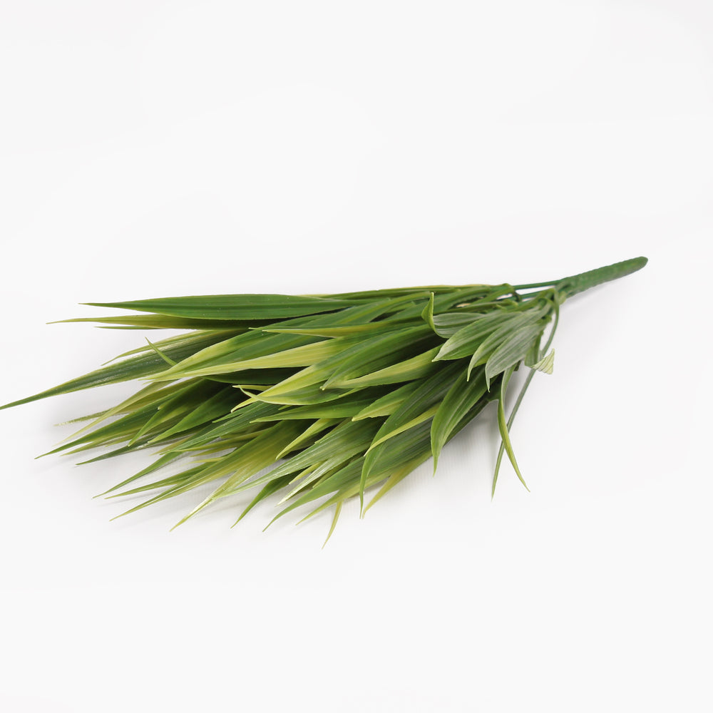 A bundle of artificial green grass or reed leaves with a green stem, photographed on a plain white background.