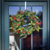 Christmas wreath with greenery, red berries, and pinecones on a glass door.
