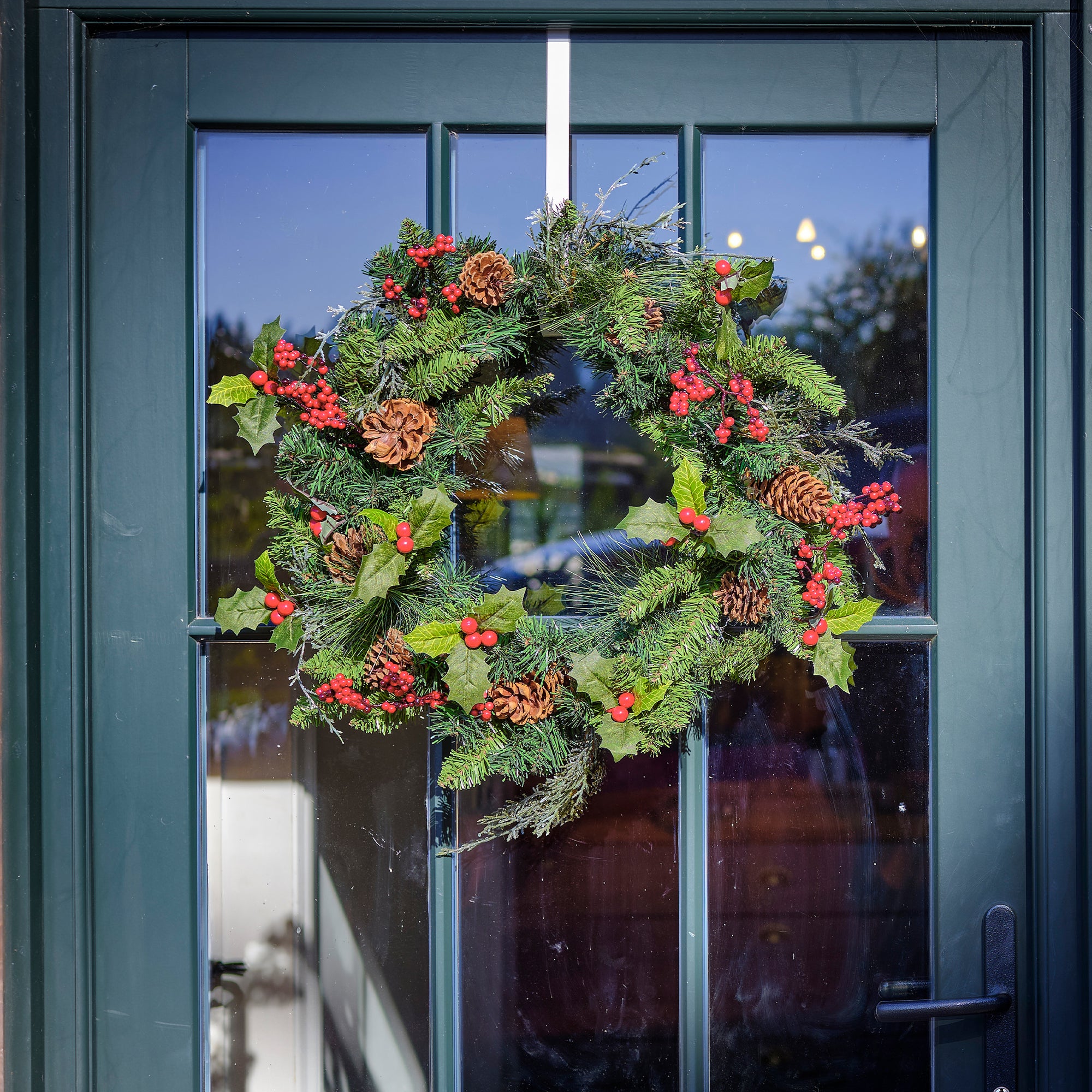 Christmas wreath with greenery, red berries, and pinecones on a glass door.