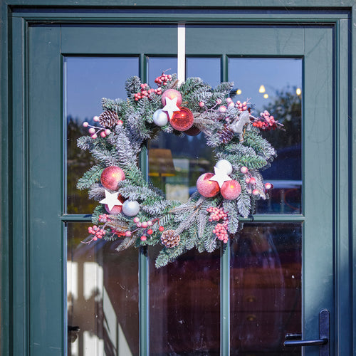 Decorative Christmas wreath with colorful ornaments hanging on a glass door.